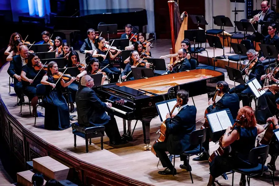 The same scene from the concerto for piano and orchestra, framed slightly tighter and darker at the edges, with the cellist seen from behind in the foreground.