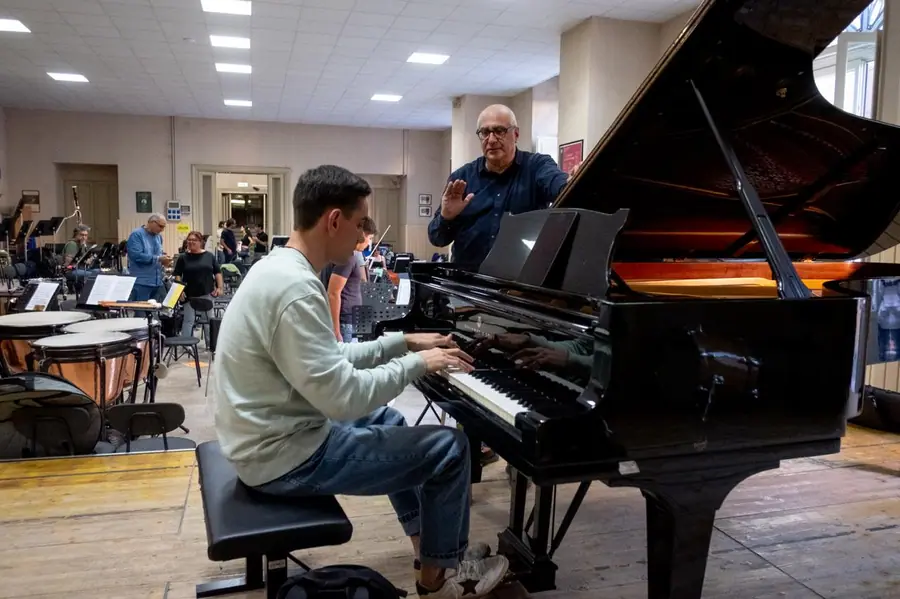 In the rehearsal room he raises a hand to point out a passage to the young pianist at the grand piano, timpani and orchestra behind
